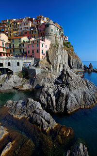 Rock formation by sea and buildings against clear blue sky