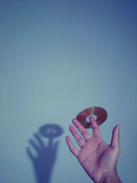 Cropped hand of person holding compact disc against wall