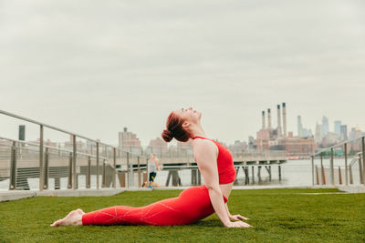 Side view of woman with arms outstretched against built structure