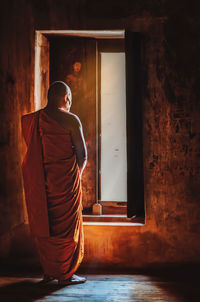 Rear view of monk wearing traditional clothing standing in temple