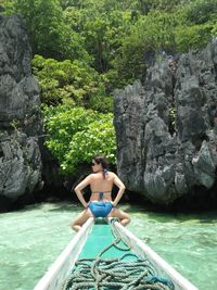 Rear view of woman wearing bikini while sitting on boat in sea against trees