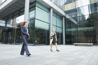 Colleague talking while walking against office building exterior