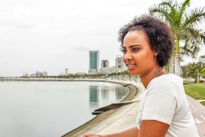 Portrait of smiling young woman by river against sky