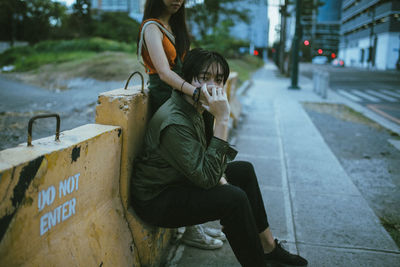 Woman with hand covering man mouth while standing on footpath in city