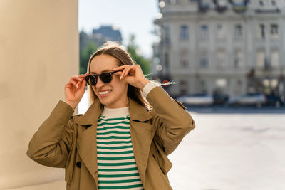 Smiling woman puts on sunglasses outside in the city