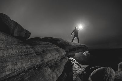 Silhouette man standing on rock against sky