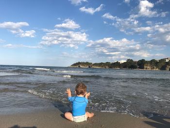 Rear view of baby sitting at beach against sky