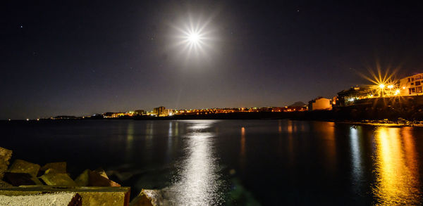 Illuminated city by sea against sky at night