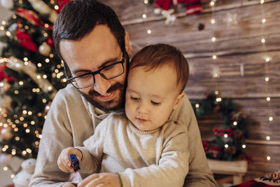 Father holding and playing with his son in living room decorated by christmas tree