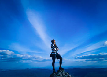 Man standing on rock against blue sky