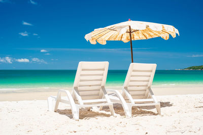 Deck chairs on beach against blue sky