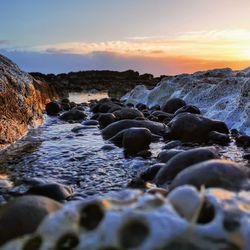 Rocks in sea against sky during sunset