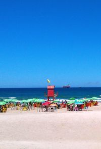 People on beach against clear blue sky