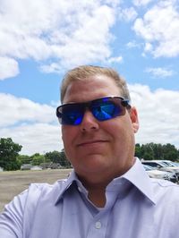 Portrait of mature man wearing sunglasses against cloudy sky