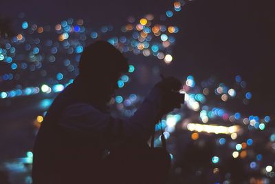 Silhouette teenage boy with camera against illuminated city at night