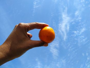 Low angle view of hand holding orange blue sky