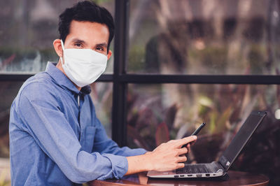 Man wearing mask using laptop at desk
