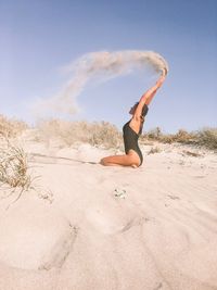 Side view of teenage girl throwing sand while sitting at beach during summer