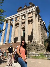 Young woman sitting on historical building against sky