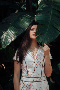 Portrait of beautiful young woman standing against tree in park