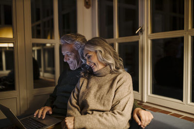 Senior couple using laptop on couch at home at night