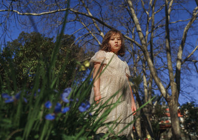 Low angle view of girl standing against bare trees in spring