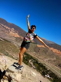Woman jumping on mountain against clear sky