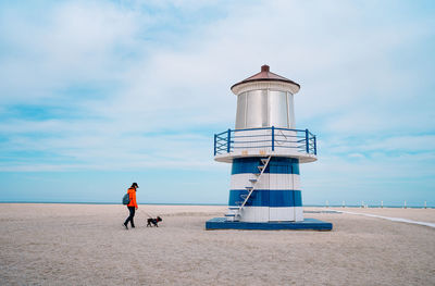 Pet owner and french bulldog dog walking on the beach by small lighthouse