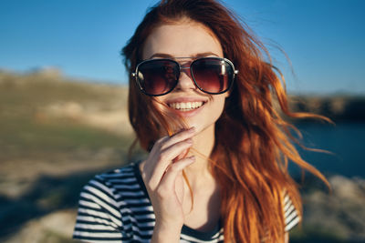 Portrait of smiling young woman wearing sunglasses against sky