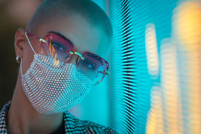 Portrait of young woman with shaved head wearing mask standing against abstract backgrounds