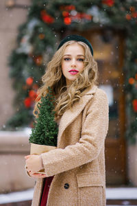 A young beautiful girl in a beige coat and a burgundy skirt is walking through a snowy city