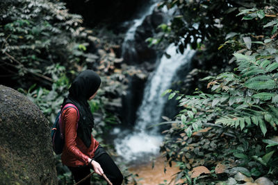 Teenage girl holding rope while standing by waterfall