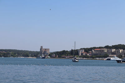 Sailboats in river by buildings against clear blue sky