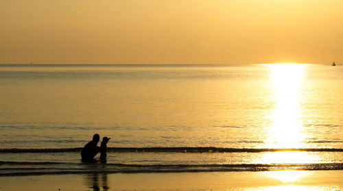 Silhouette people on sea against sky during sunset