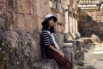 Young pretty asian girl sits on the foundation of an ancient hindu temple ruins