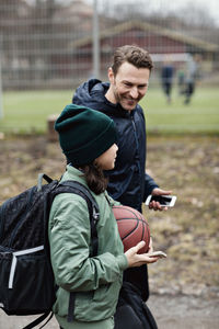 Smiling father and son talking while walking on street after basketball practice in winter