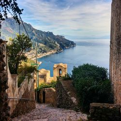 Scenic view of sea by mountain against cloudy sky