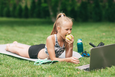 Girl with laptop eating apple on field