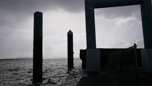 Wooden posts in sea against sky