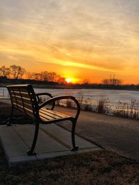 Empty bench by sea against sky during sunset