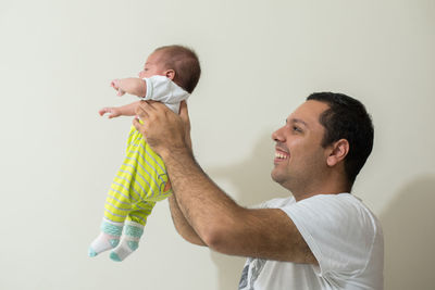 Smiling father carrying son while standing against wall