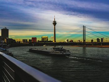 Nautical vessel on river by buildings against sky during sunset