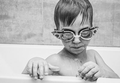 Shirtless boy wearing swimming goggles bathing in bathtub