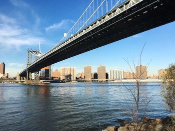 Low angle view of manhattan bridge over east river in city against blue sky