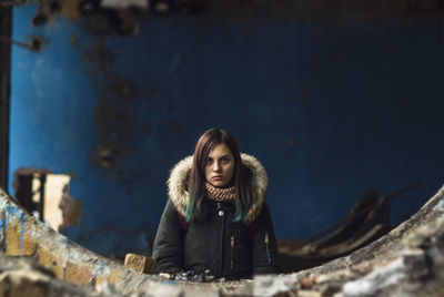 Portrait of young woman in warm clothes standing at abandoned building