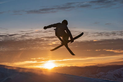 Snow skier jumping through sunset.