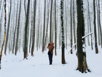 Full length of woman standing in snow covered forest