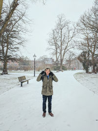 Portrait of man standing on snowy road against bare trees