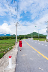 Rear view of woman walking on road against sky