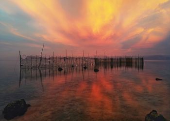 Wooden posts in sea against sky during sunset